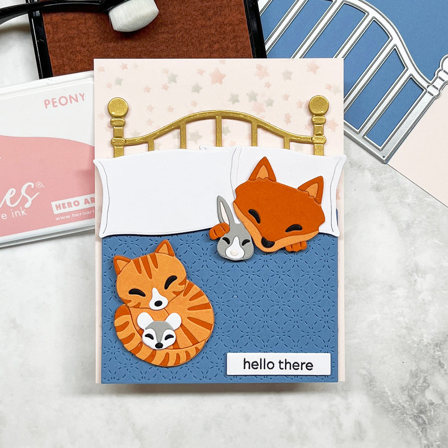 Handmade card featuring a die cut fox and orange tabby cat in  a brass bed  with a blue quilt.